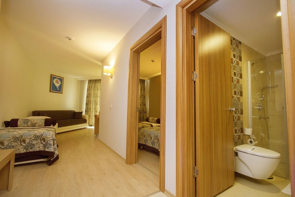 A hotel room with a wooden floor, a sofa, a bed, a bathroom with a shower, and a toilet.