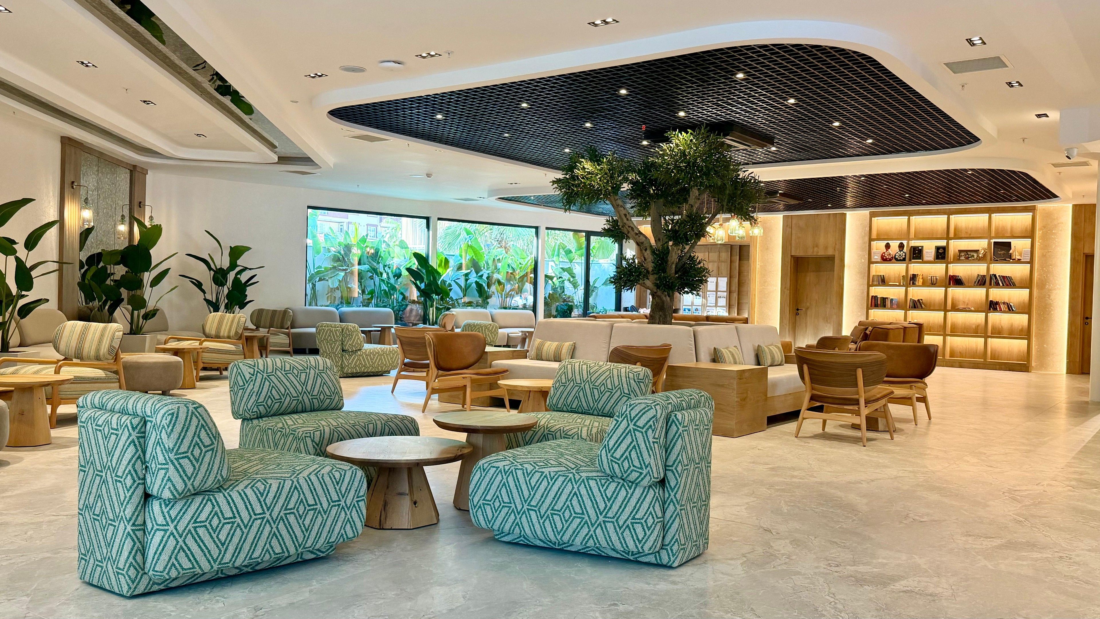 Ein stilvoller Lounge-Bereich mit Sofas, Sesseln und einem zentralen Couchtisch, mit einem großen Fenster und Blick ins Grüne.