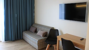 Una habitación con un sofá a cuadros, una silla negra, un escritorio de madera y un televisor de pantalla plana en la pared.
