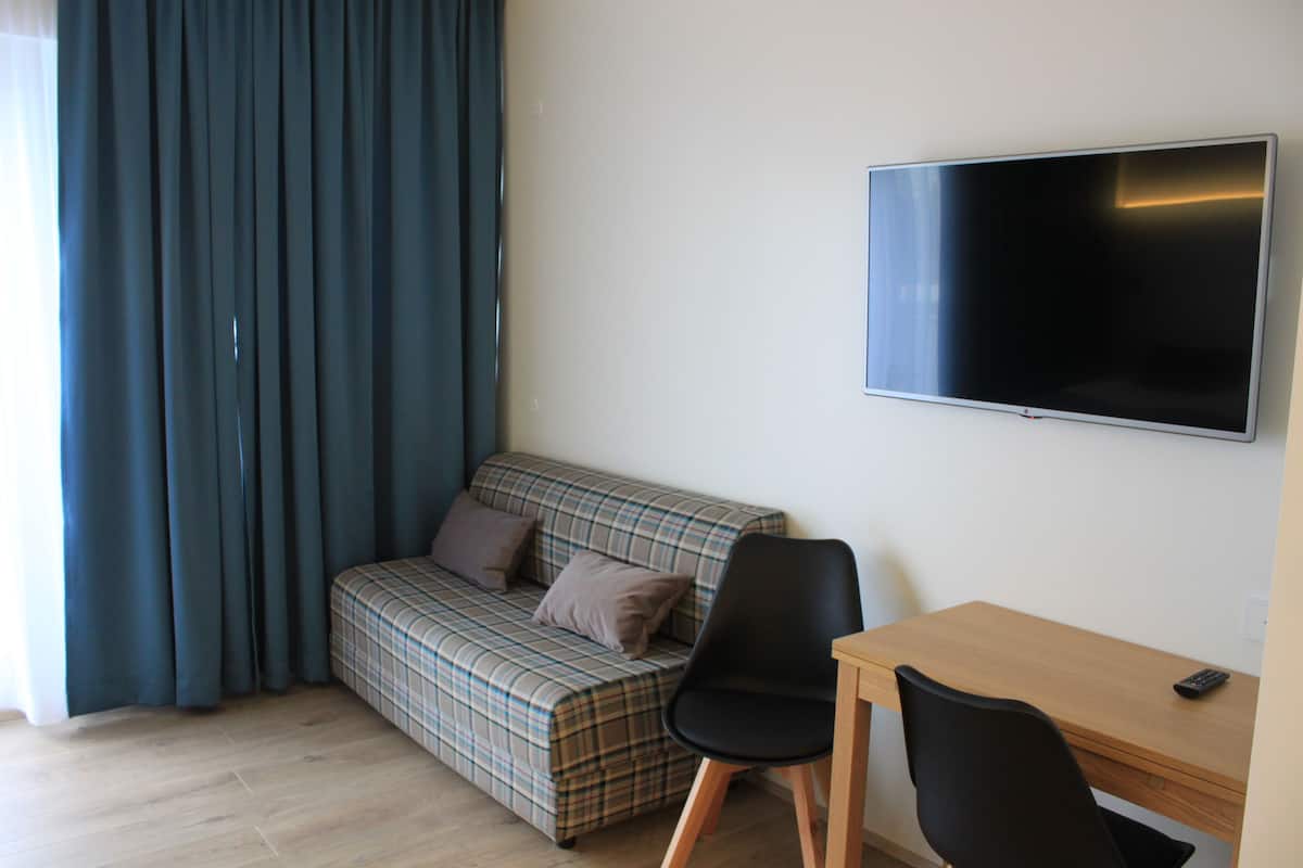 A room with a plaid sofa, a black chair, a wooden desk, and a flat-screen TV on the wall.