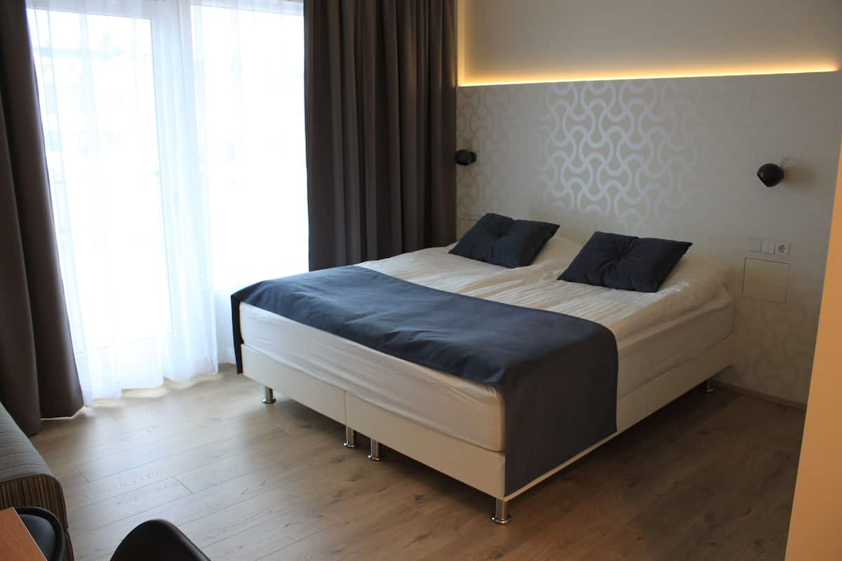 A modern hotel room with a large bed, a bedside table, and a window with curtains.