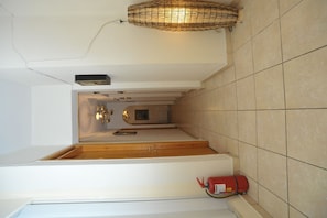 A staircase with a fire extinguisher on the landing, a small shelf with a box, and a wall-mounted light fixture. - Hera Hotel (Nafplio)