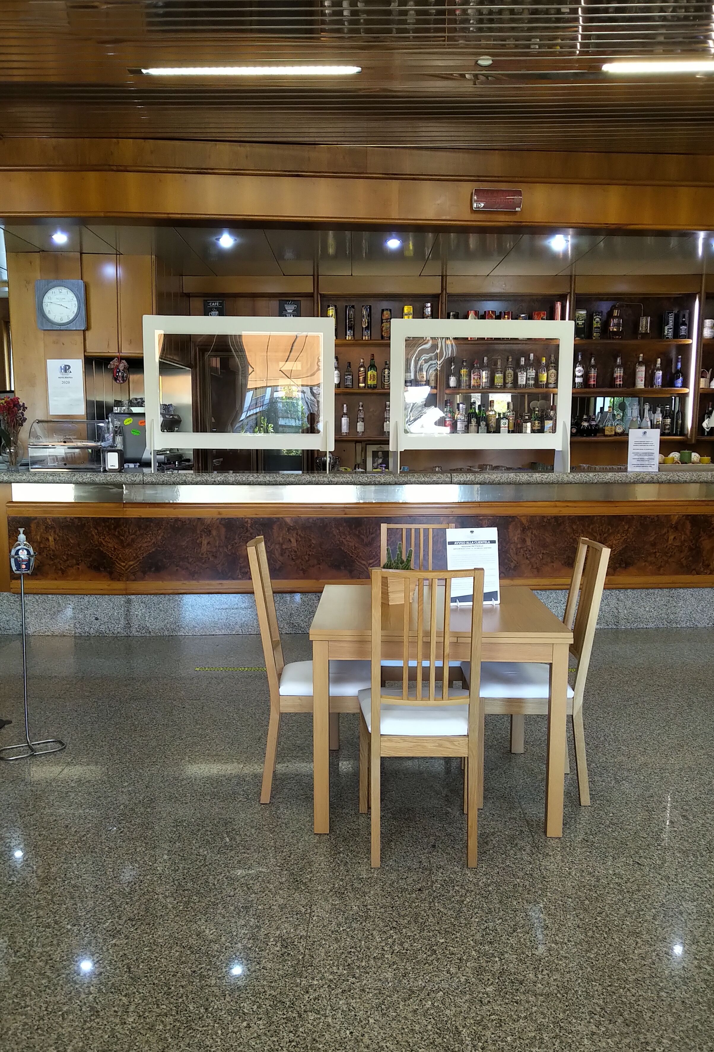 Zona de bar con mostrador de madera, un reloj y estantes con botellas.