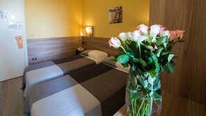 A hotel room with two beds, a vase of flowers, a nightstand, and a wall-mounted lamp. - Hotel Route 9 (Cadeo)