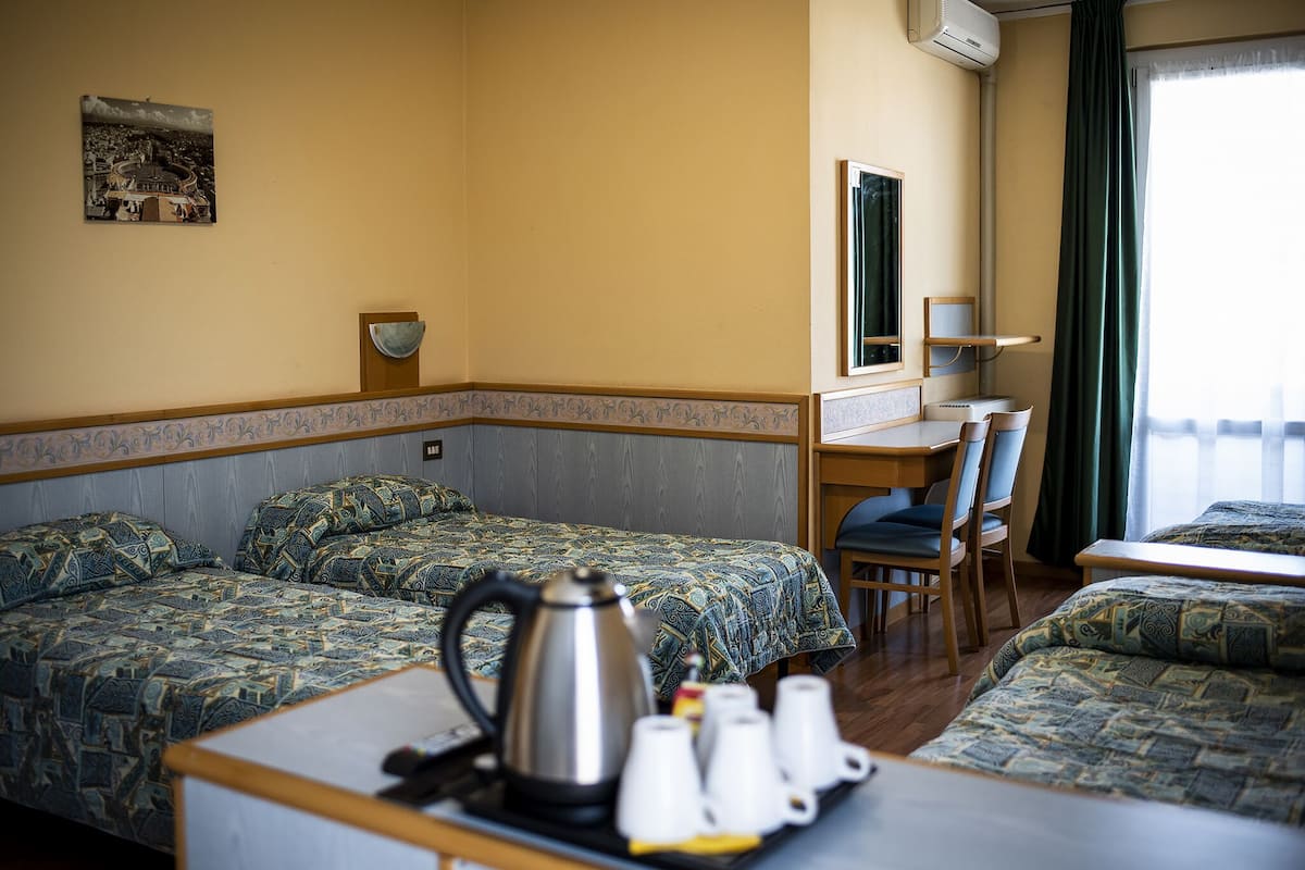 A hotel room with two beds, a desk, a chair, a coffee maker, and a tray with cups.