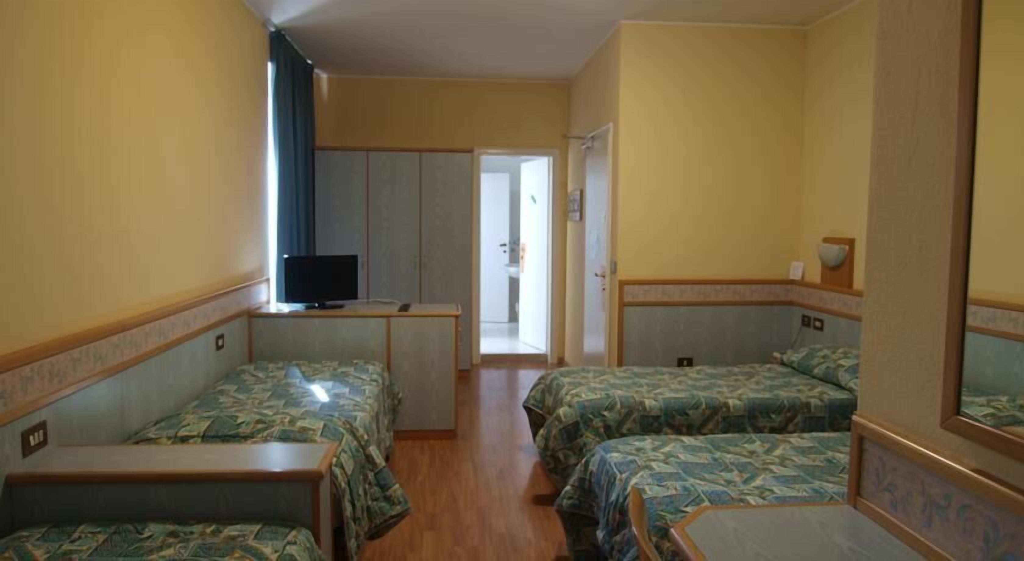 Ein kleines Hotelzimmer mit zwei Einzelbetten, einem kleinen Schreibtisch, einem Fernseher und einem Kleiderschrank.