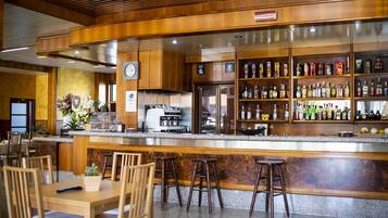 Zona de bar con mobiliario de madera, una máquina de café y estanterías llenas de diferentes botellas.
