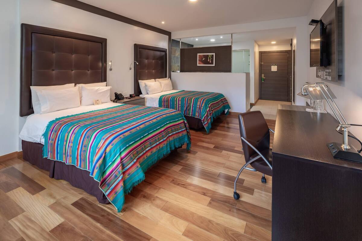 A hotel room with two beds, a desk, and a chair.