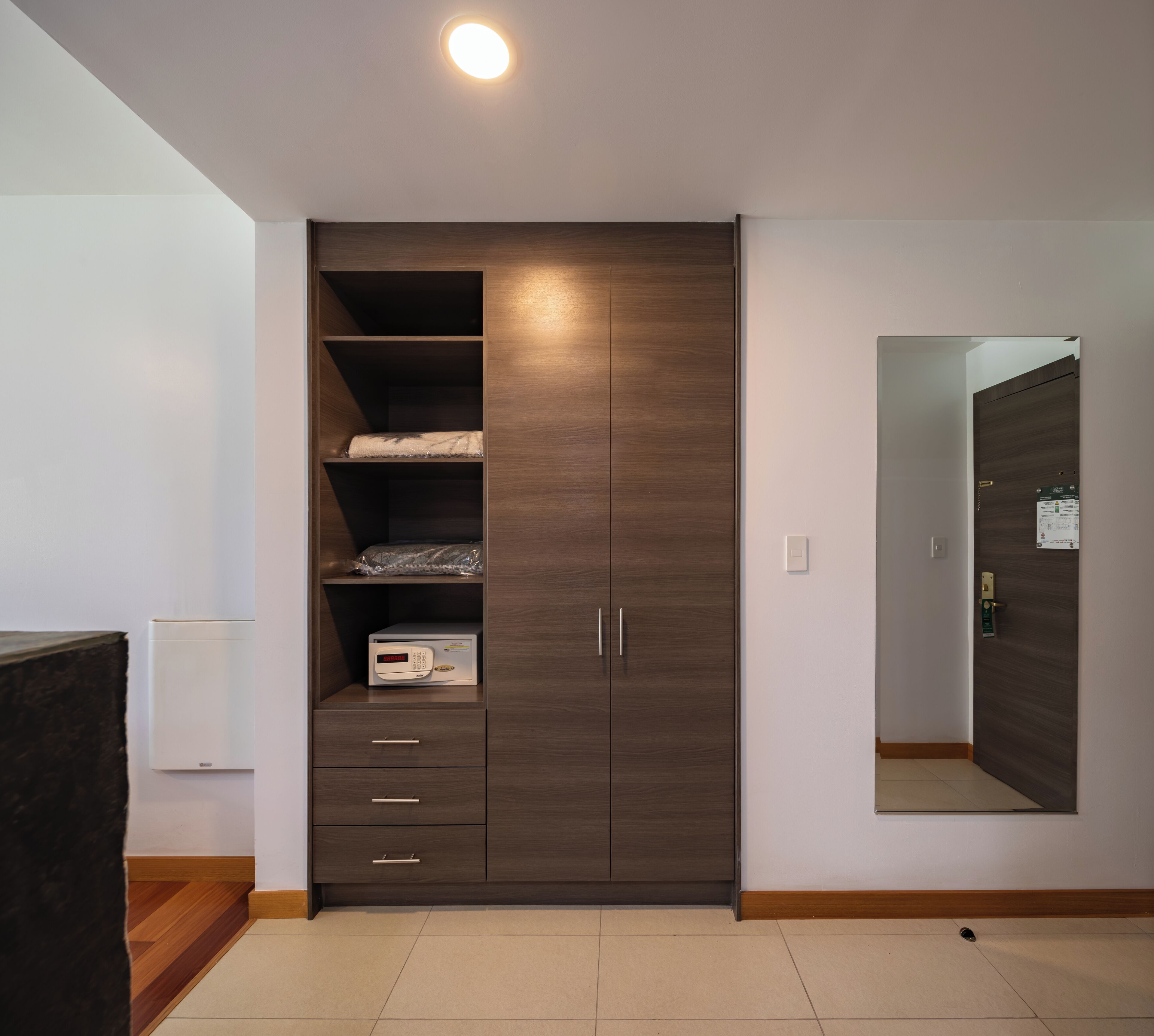 A modern bedroom with a built-in wardrobe, a mirror, and a digital clock on the wall.