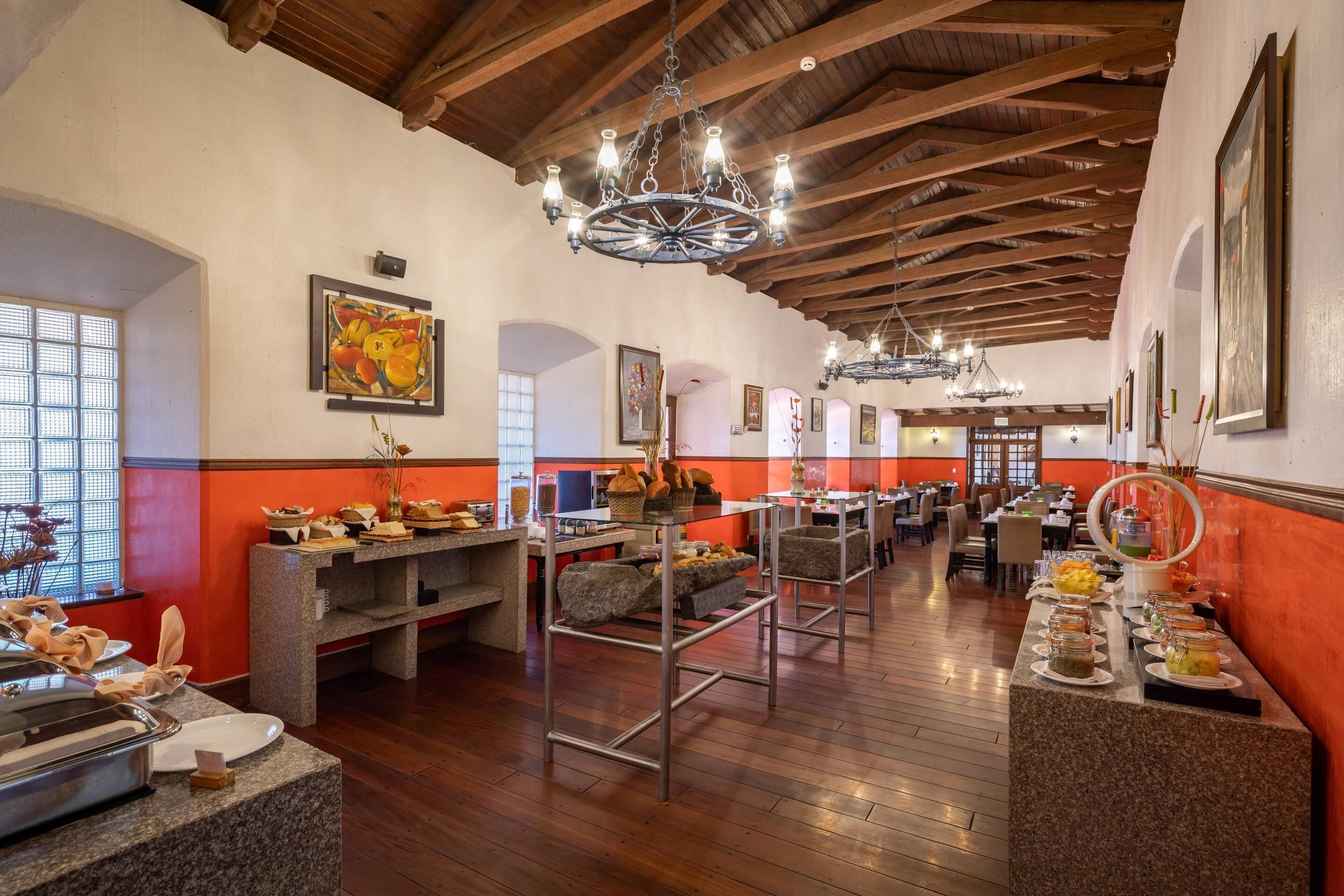 A spacious dining area with high wooden ceilings and chandeliers, featuring a buffet setup with various food items and seating arrangements.