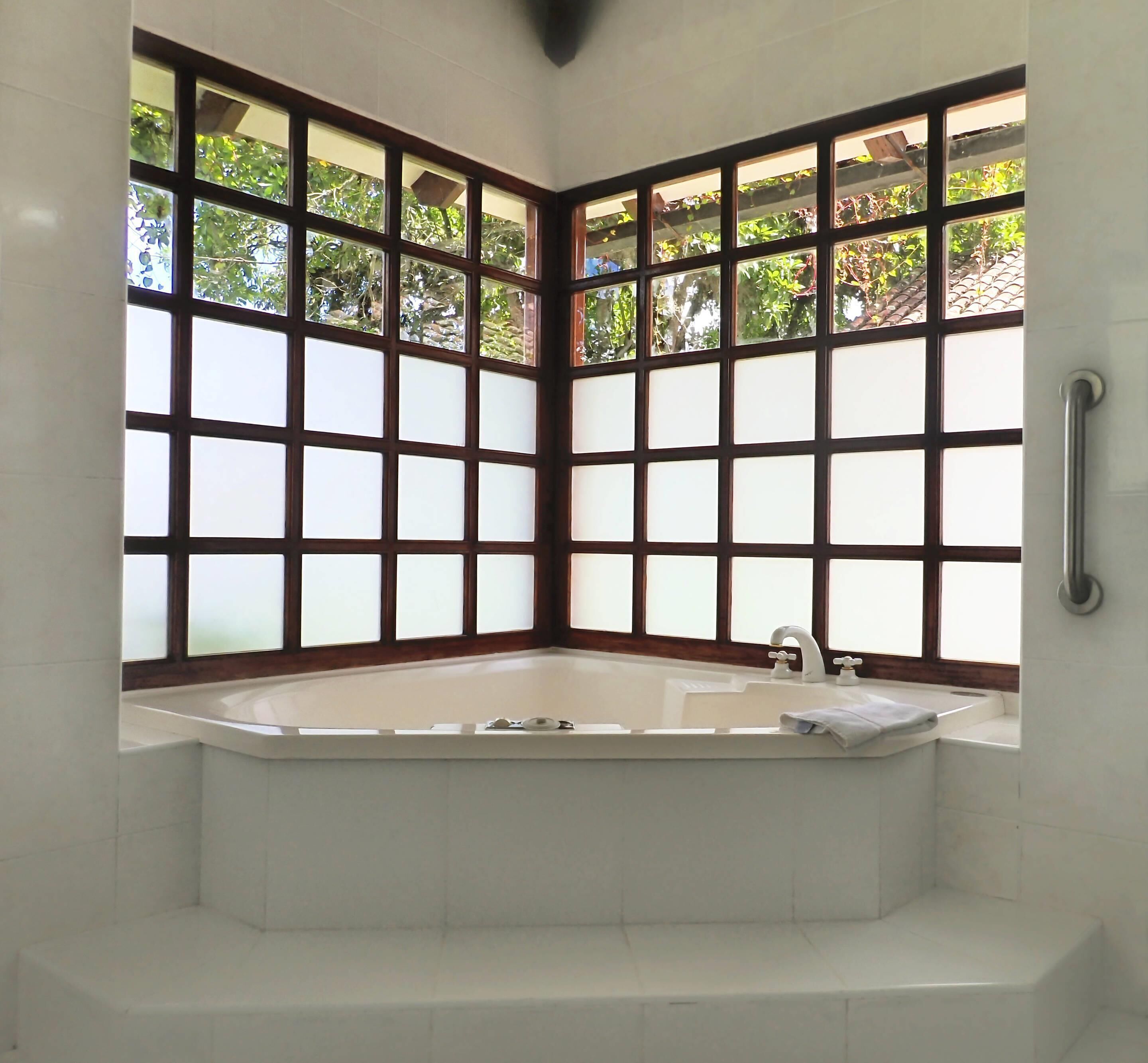 A corner bathroom with a large bathtub, frosted glass windows, and a handrail.