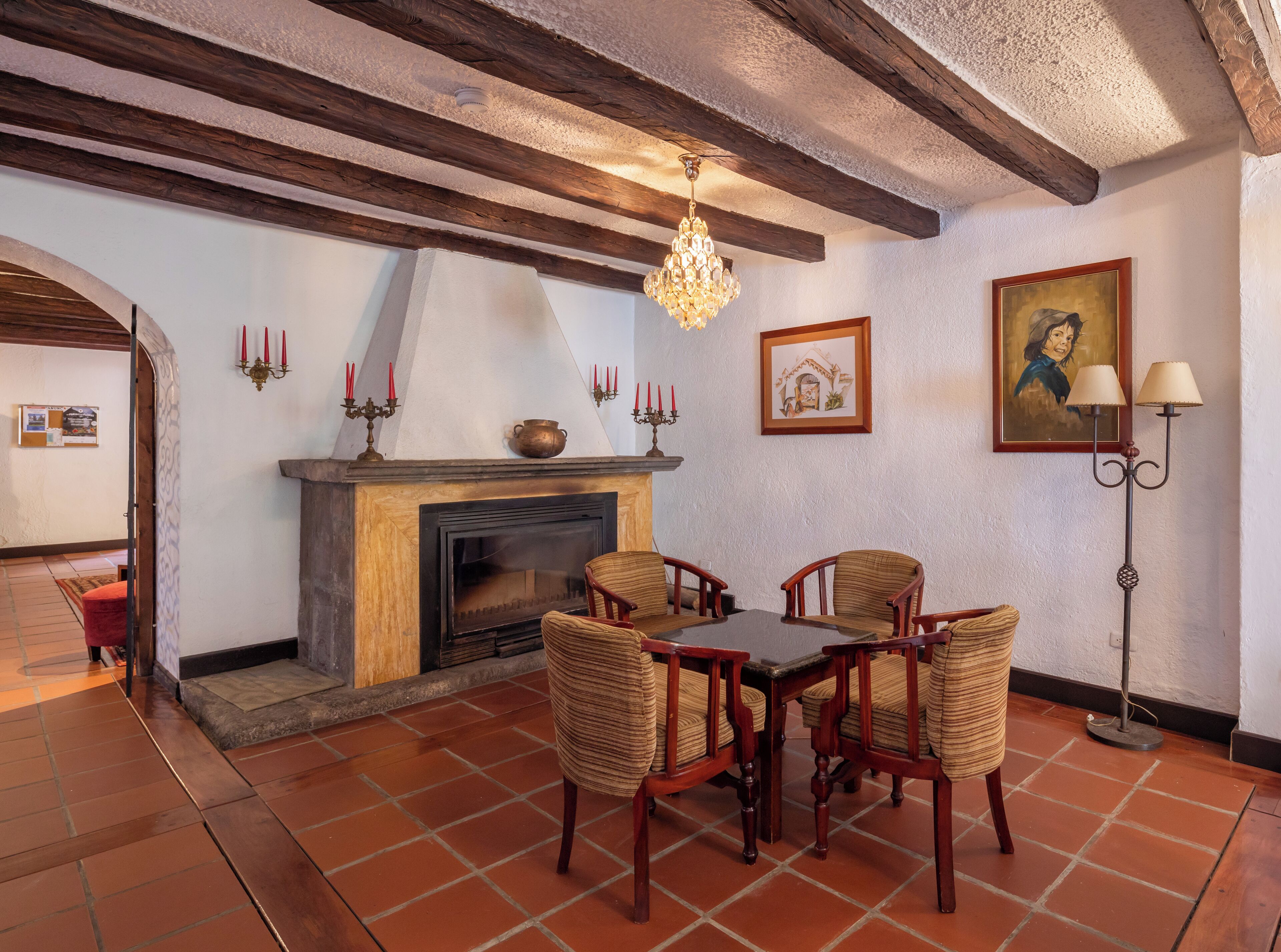 A dining area with a fireplace, wooden chairs, a table, and a chandelier.