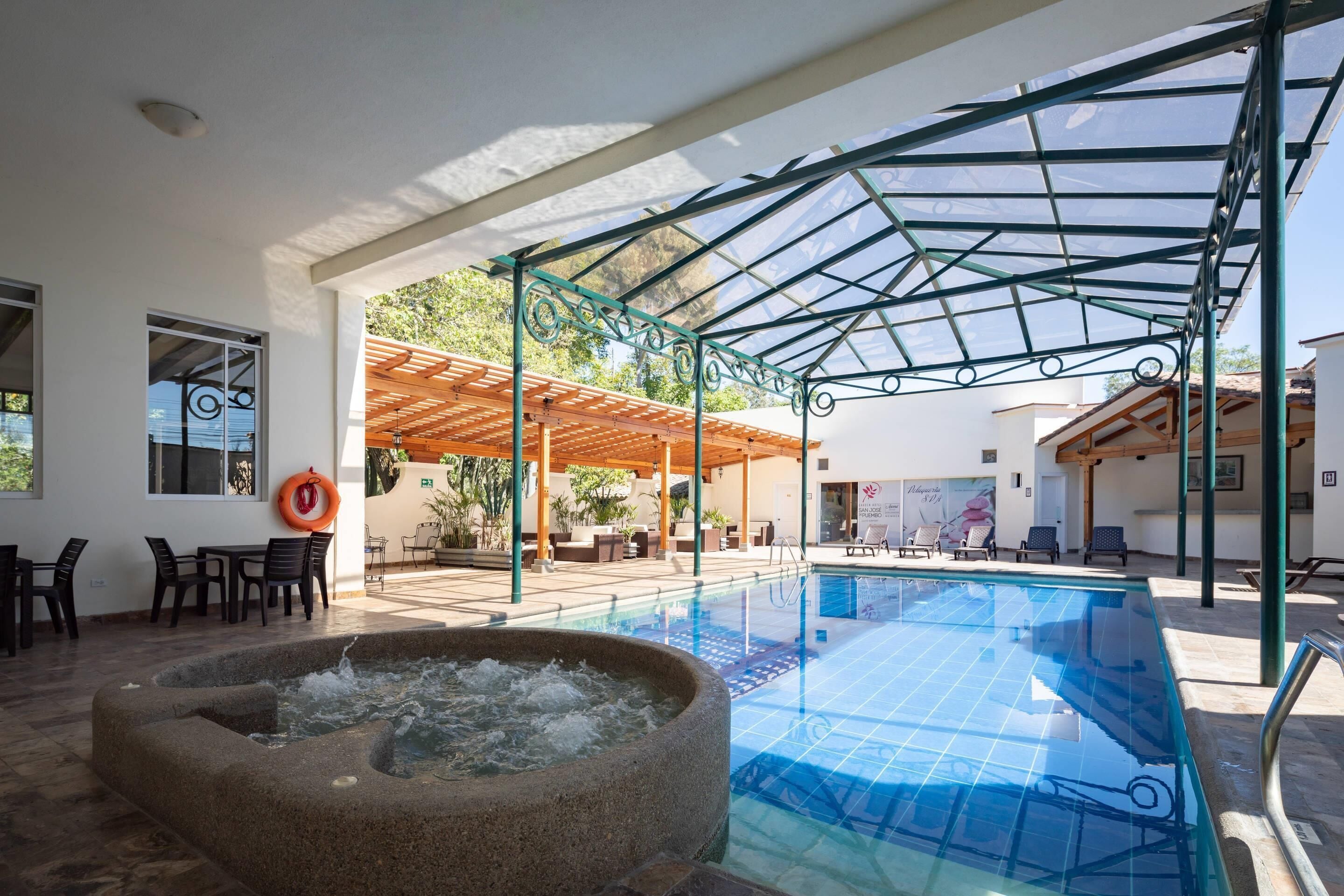 Een binnenzwembad met een stenen jacuzzi, een overdekte zithoek en uitzicht op het omliggende landschap.