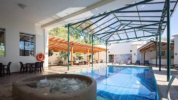 An indoor swimming pool with a stone hot tub, a covered seating area, and a view of the surrounding landscape.