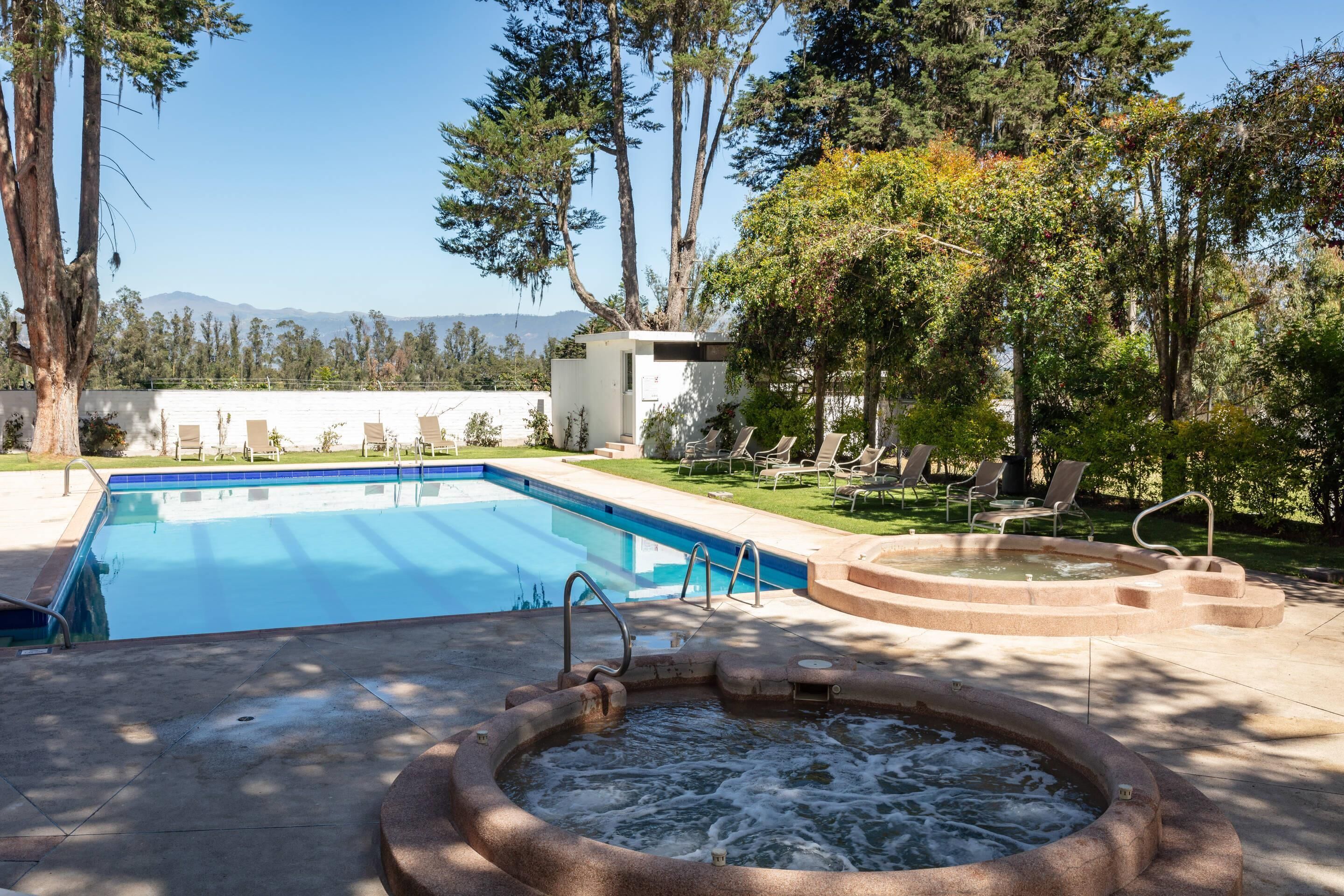 Una piscina con hidromasaje, rodeada de sillas de descanso y árboles.