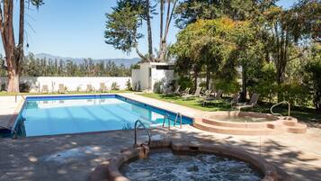 Una piscina con hidromasaje, rodeada de sillas de descanso y árboles.