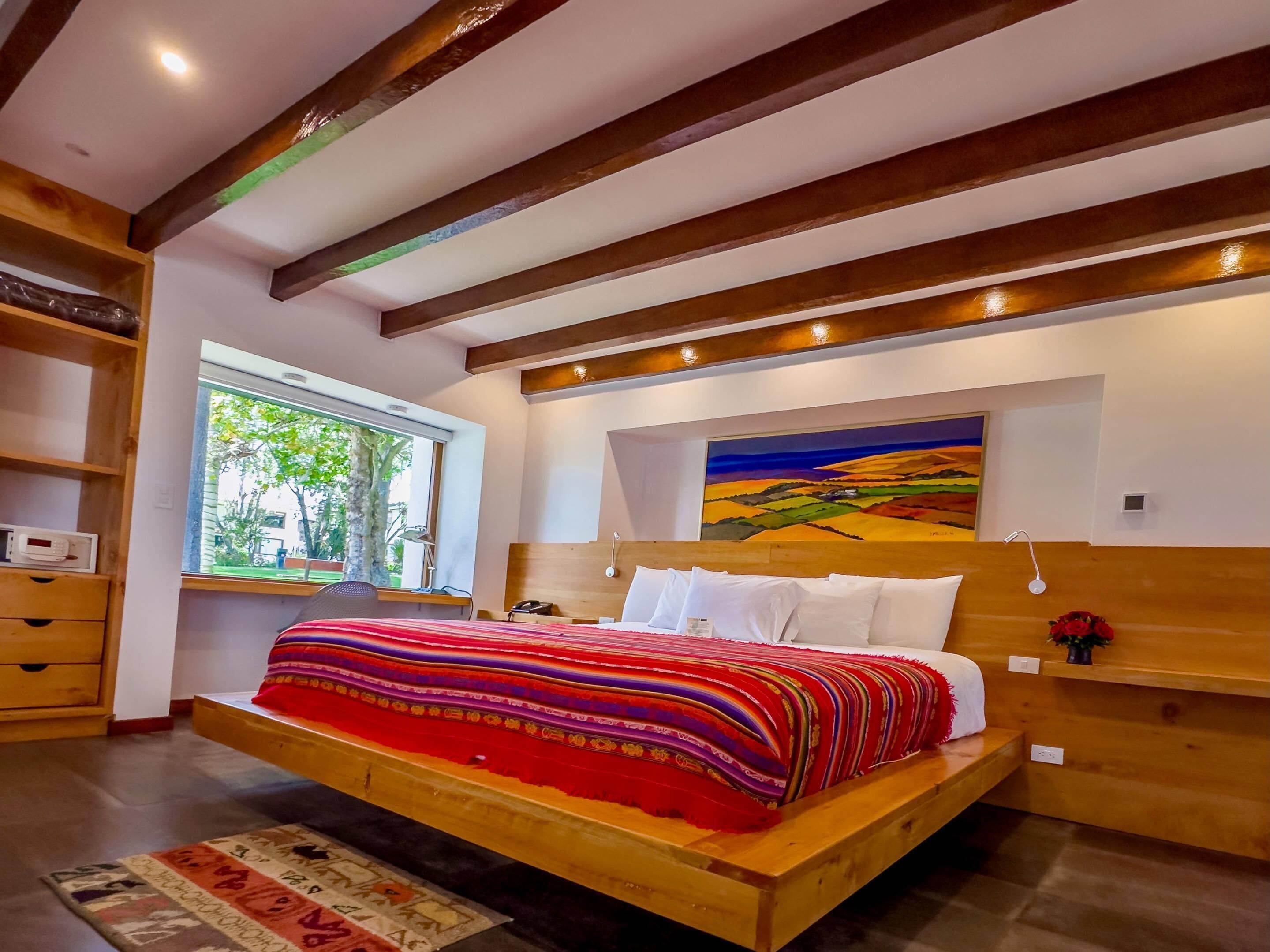 A modern bedroom with a wooden bed, a large window, and a painting on the wall.
