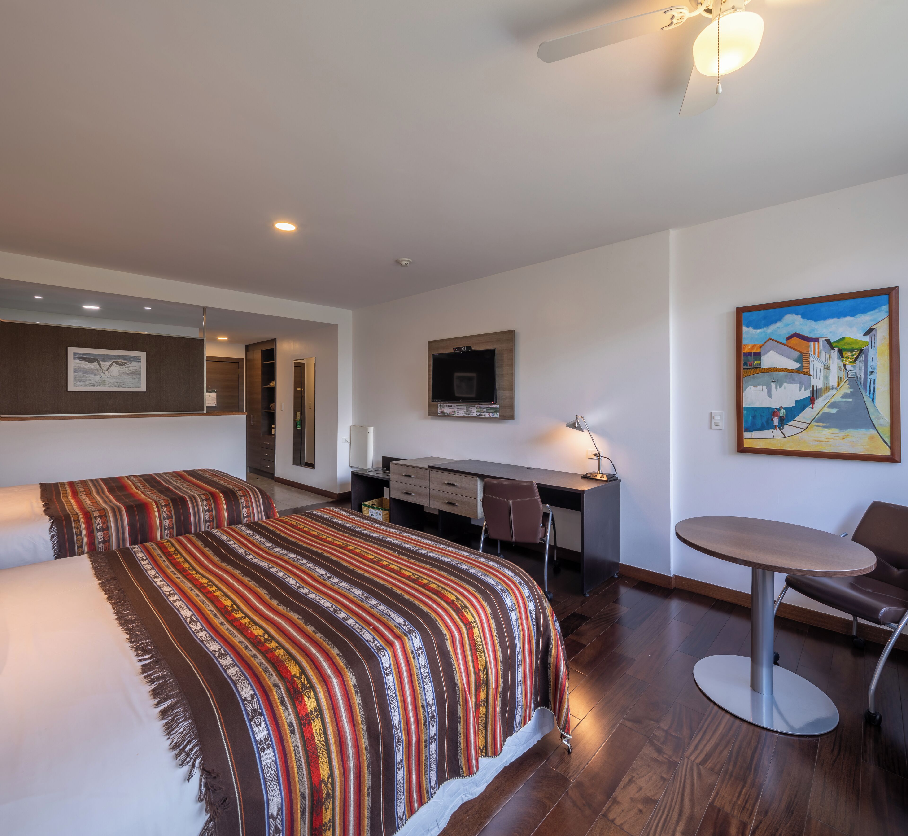 Habitación de hotel con una cama grande, un escritorio, una silla, un televisor y un cuadro en la pared.