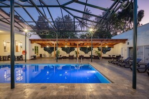 Une piscine intérieure dotée d’un espace abrité, de chaises longues et offrant une vue sur les arbres environnants.