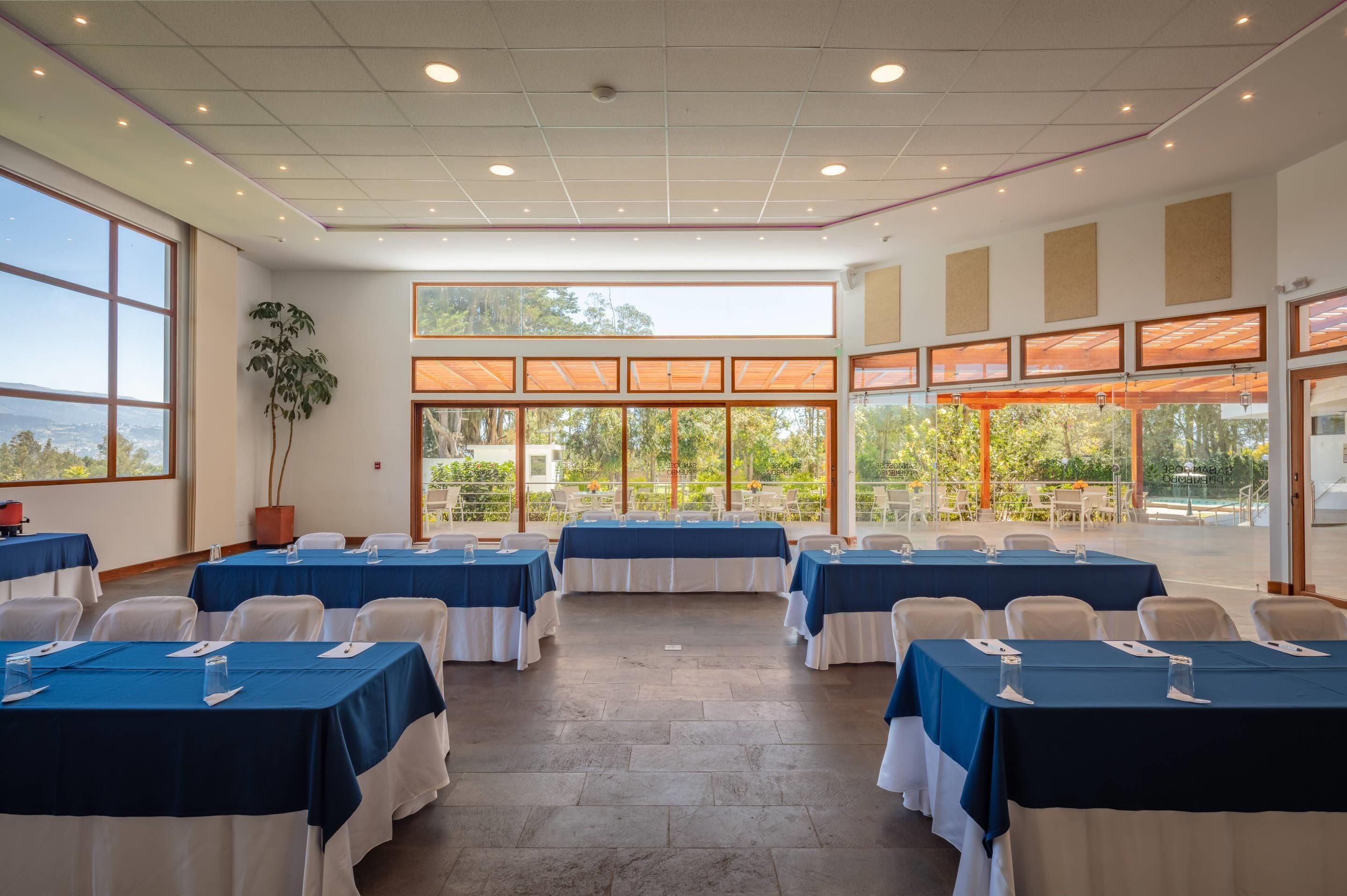 Un salón de conferencias con varias mesas, ventanas amplias y vistas al exterior.