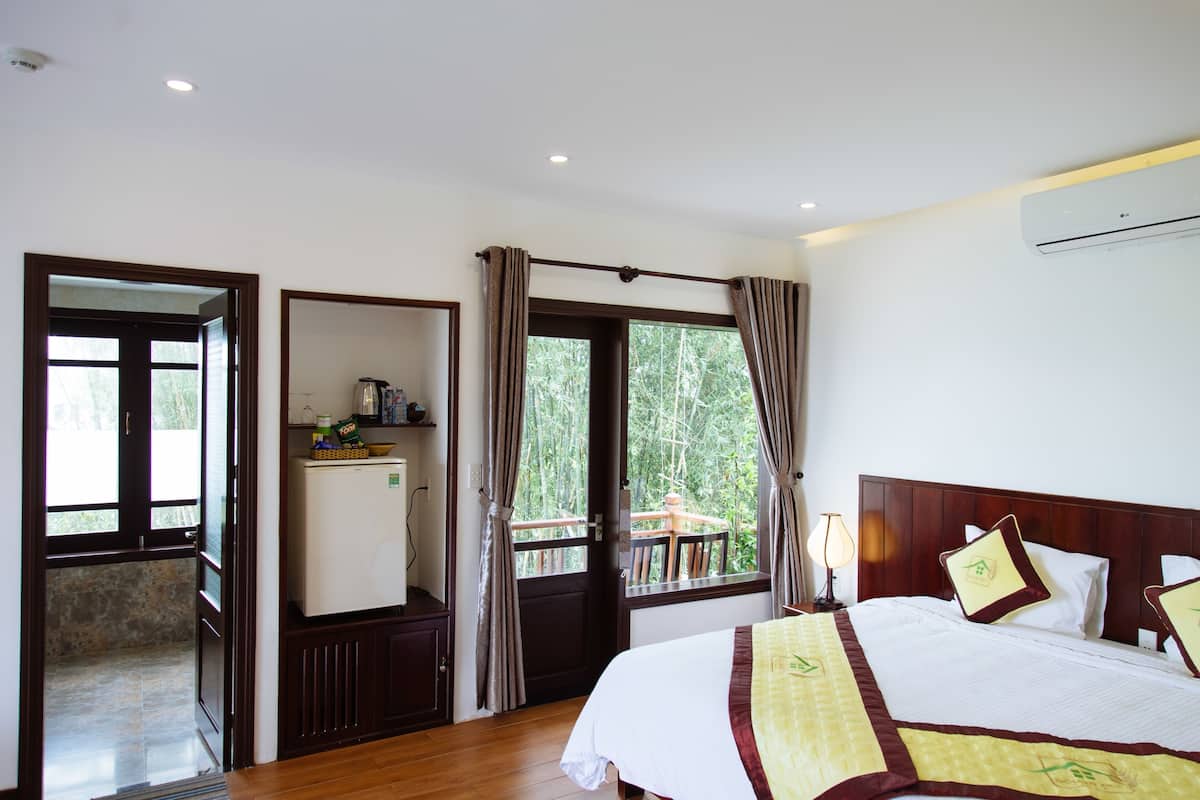 A hotel room with a bed, a desk, a refrigerator, and a balcony with curtains.