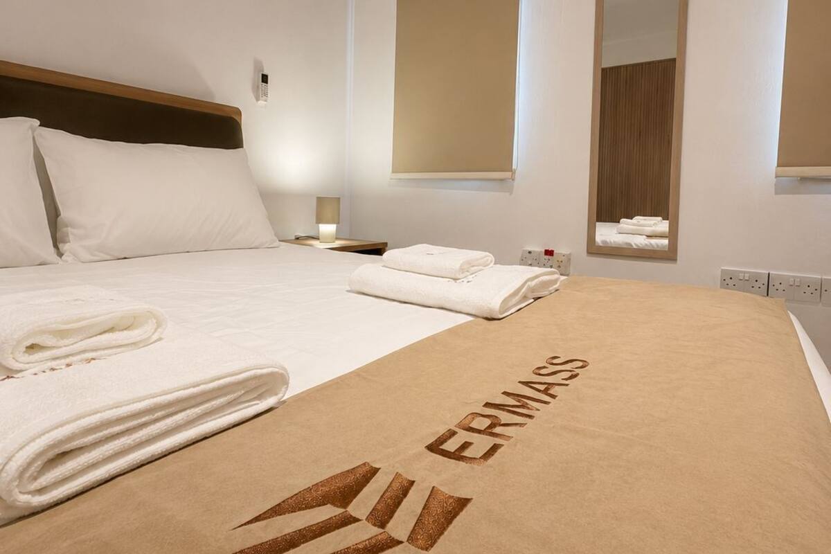 A hotel room with a bed, a large window, an air conditioning unit, and a towel on the bed.