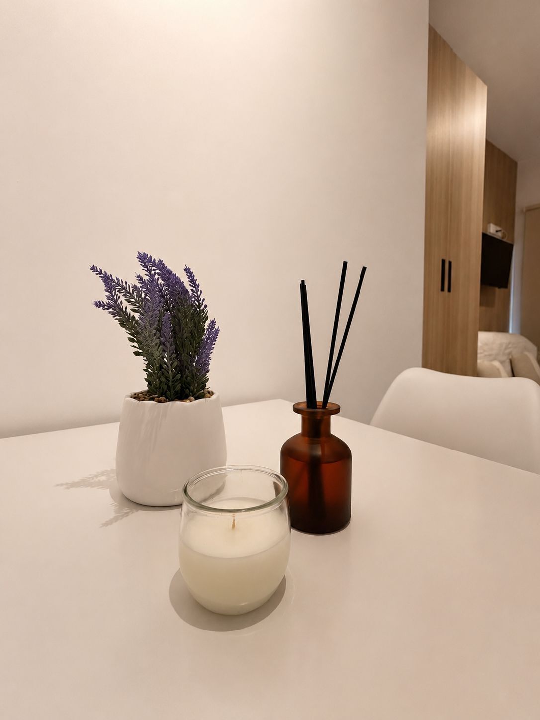 Ein weißer Tisch mit einer Topfpflanze, einer Kerze und einem Diffusor aus Schilf.