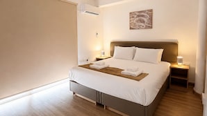 Una habitación de hotel moderna con una cama grande, lámparas de noche, un equipo de aire acondicionado y una obra de arte colgada en la pared.