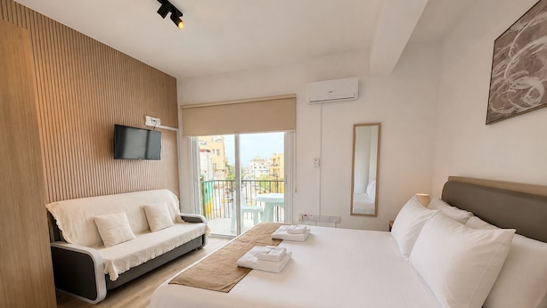 Una habitación de hotel con cama, sofá, televisor, balcón y espejo.