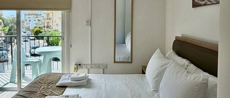 Hotelkamer met een bed, een raam met uitzicht op gebouwen, een airconditioning, een spiegel en een tafel met stoelen buiten.