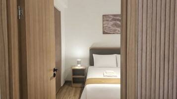 A hotel room with a wooden wardrobe, a bedside table with a lamp, a bed with white bedding, and a wall-mounted artwork.