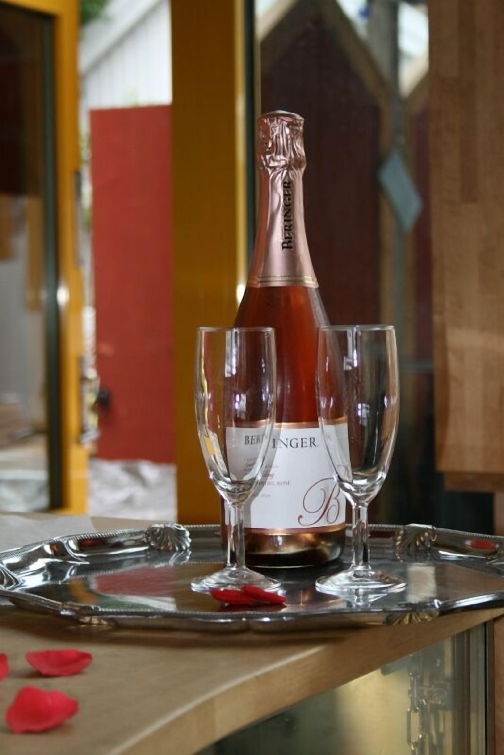 A bottle of Beringer wine on a tray with two glasses and rose petals.