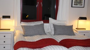 A neatly made bed with striped bedding and two pillows, a red throw blanket, and two bedside tables with lamps. - Brännö Värdshus & Pensionat Baggen (Branno)