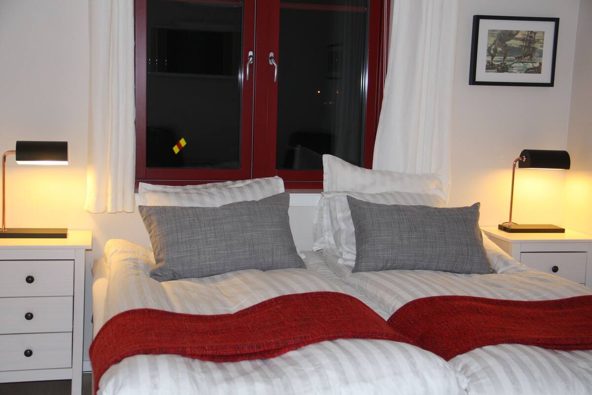 A neatly made bed with striped bedding and two pillows, a red throw blanket, and two bedside tables with lamps.