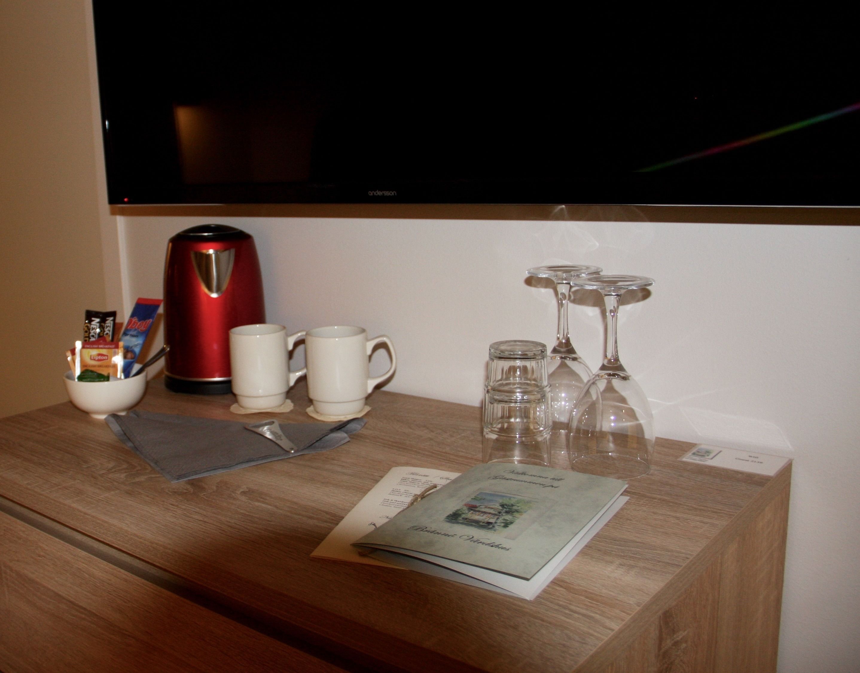 Une table en bois avec une cafetière rouge, deux tasses blanches, un menu et des verres à vin.