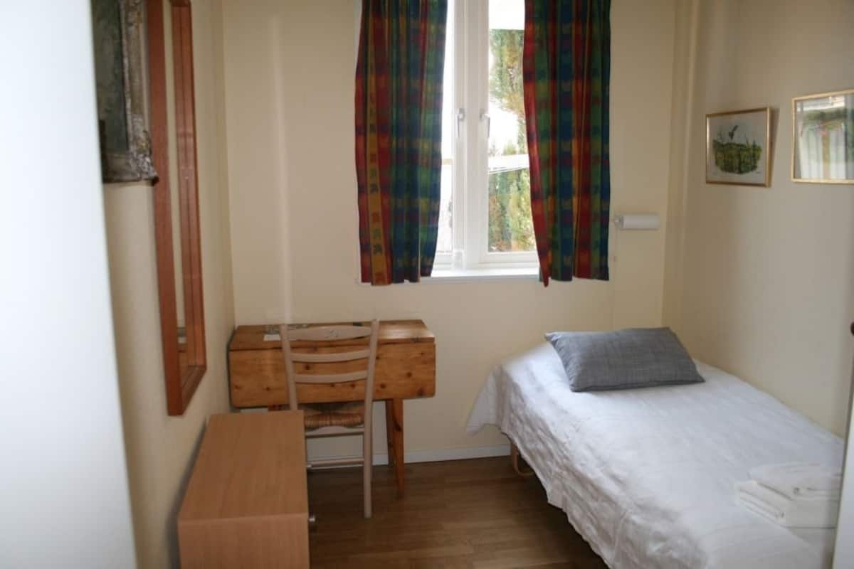 A small, tidy room with a single bed, a wooden desk, and a chair.