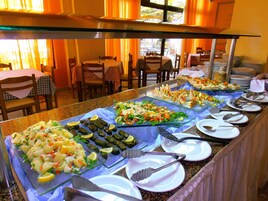Un bufé con diversos platos, como ensaladas, carnes y verduras, en un comedor bien iluminado con mesas y sillas.