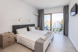 Habitación de hotel con cama doble, mesitas de noche, un escritorio pequeño, una silla y un balcón con mesa y sillas.