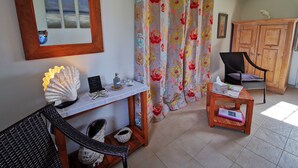 Una habitación con una silla de madera, una mesa pequeña con una concha decorativa, un espejo y un mueble de madera.