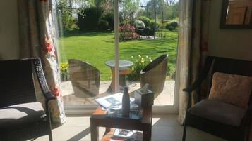 A room with a view of a well-maintained garden, wicker furniture, and a small table with magazines.