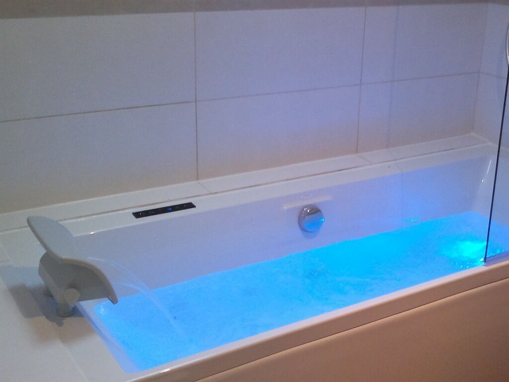 A modern bathtub with a glass enclosure and a blue light feature.