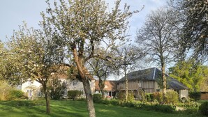 Un edificio tradicional con un jardín amplio, un árbol en flor y un césped bien cuidado.