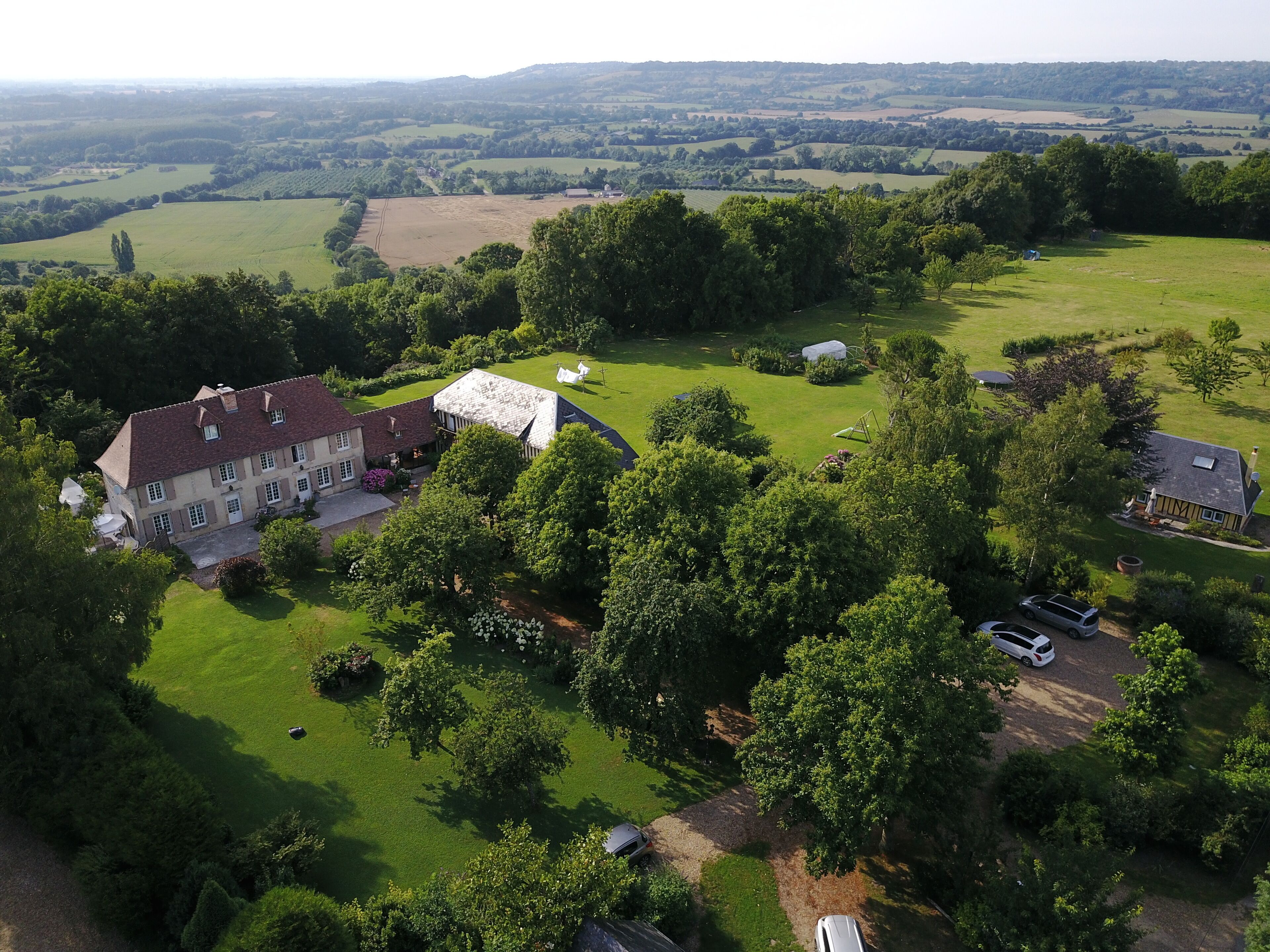 Luchtbeeld van een landgoed met een groot huis, uitgestrekte groene velden en enkele geparkeerde auto's.