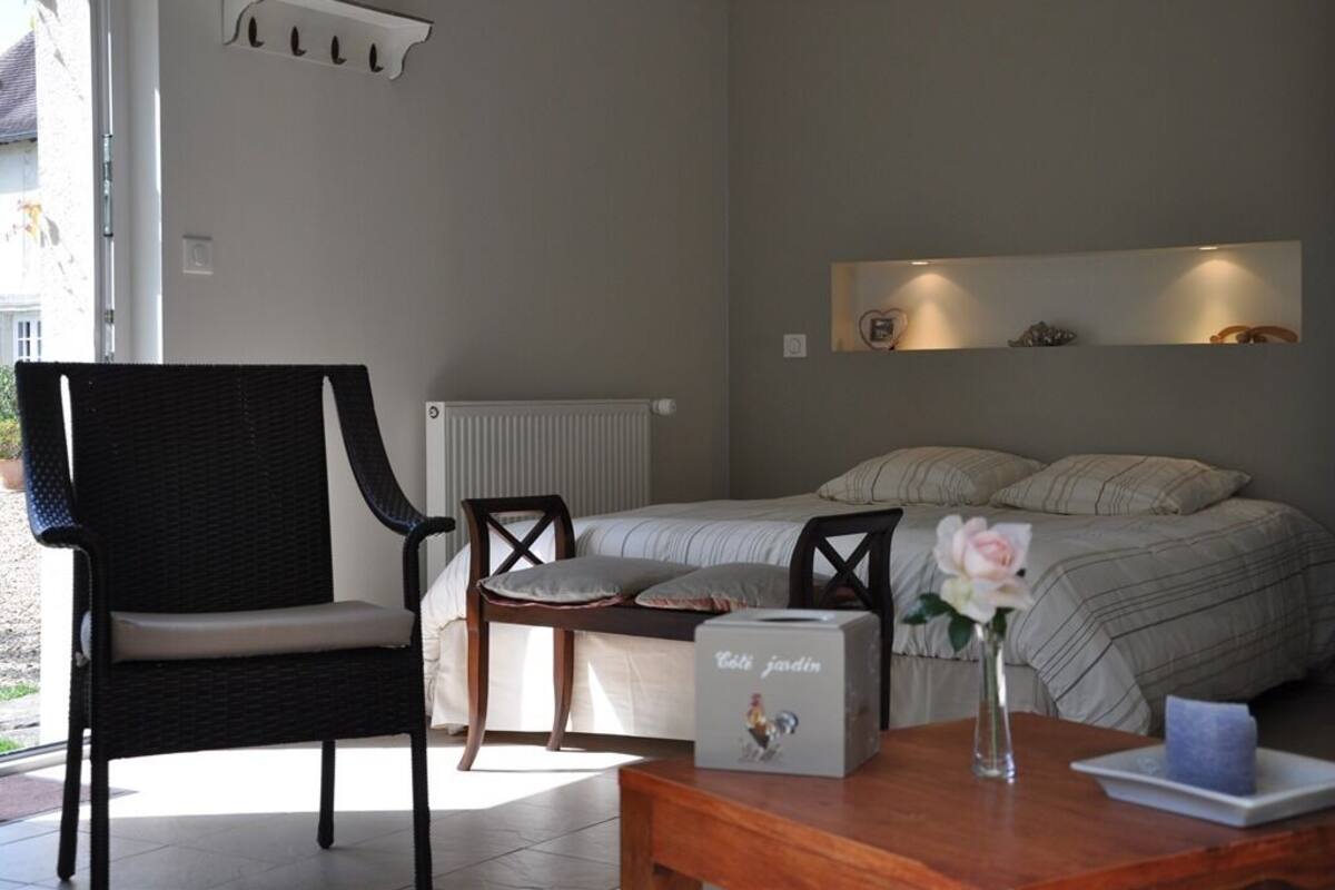 A bedroom with a bed, a chair, a table, and a bedside table with a vase.