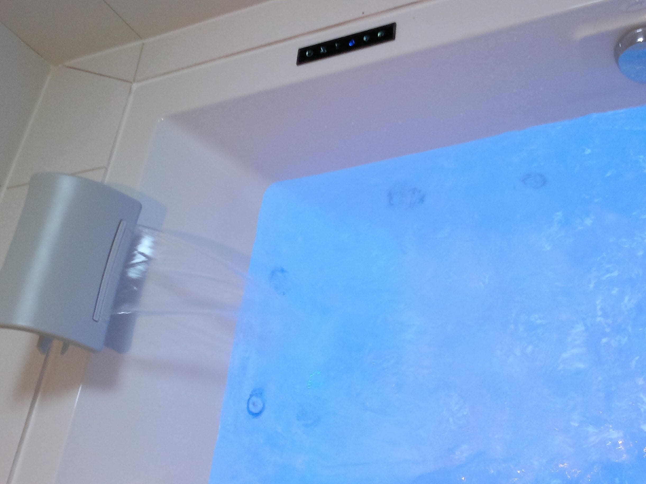 Una vasca da bagno con idromassaggio, un pannello di controllo e una parete piastrellata.