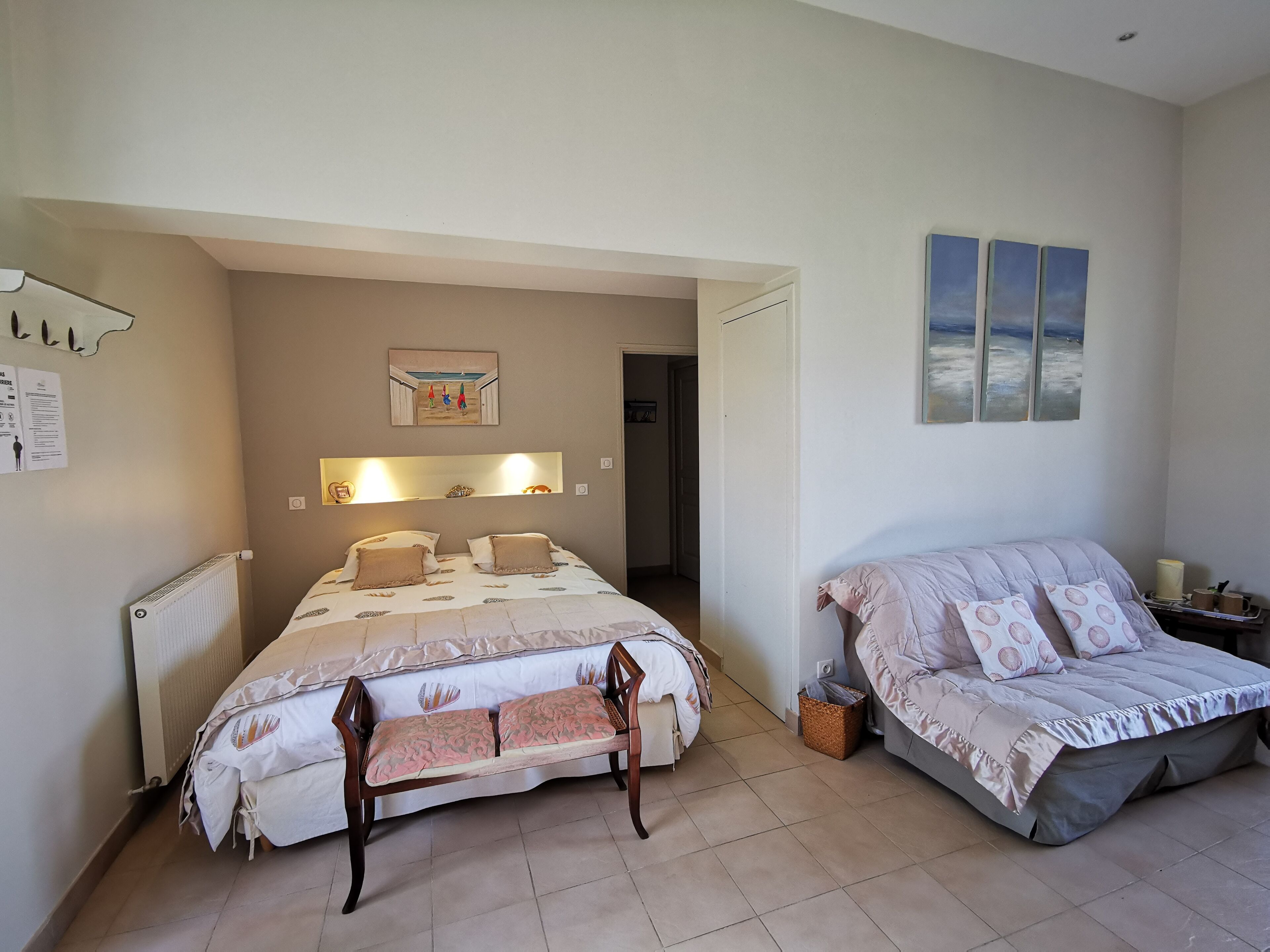 Un dormitorio con cama, un banco, una mesita de noche y un estante en la pared.