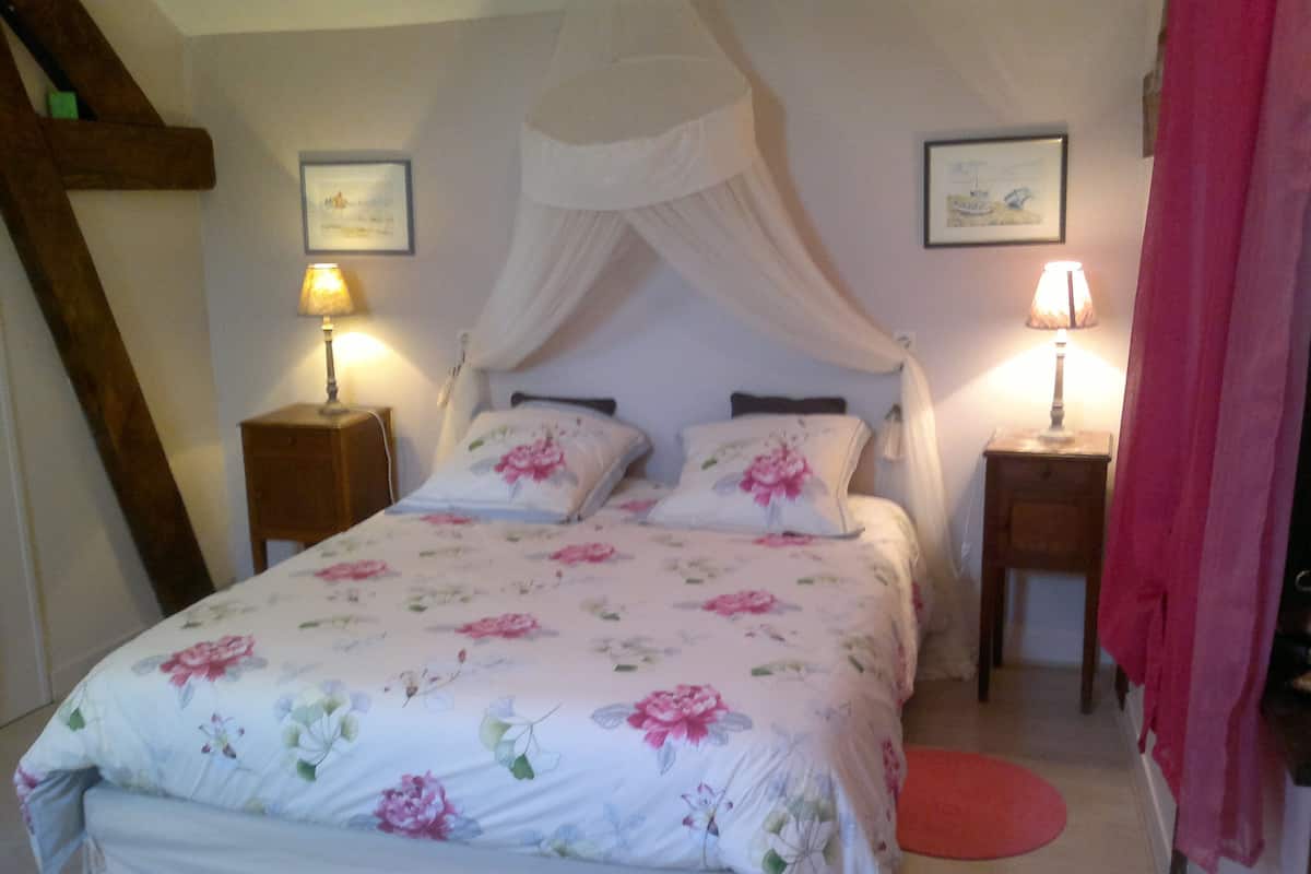 A bedroom with a canopy bed, floral bedding, two bedside lamps, and framed artwork on the walls.