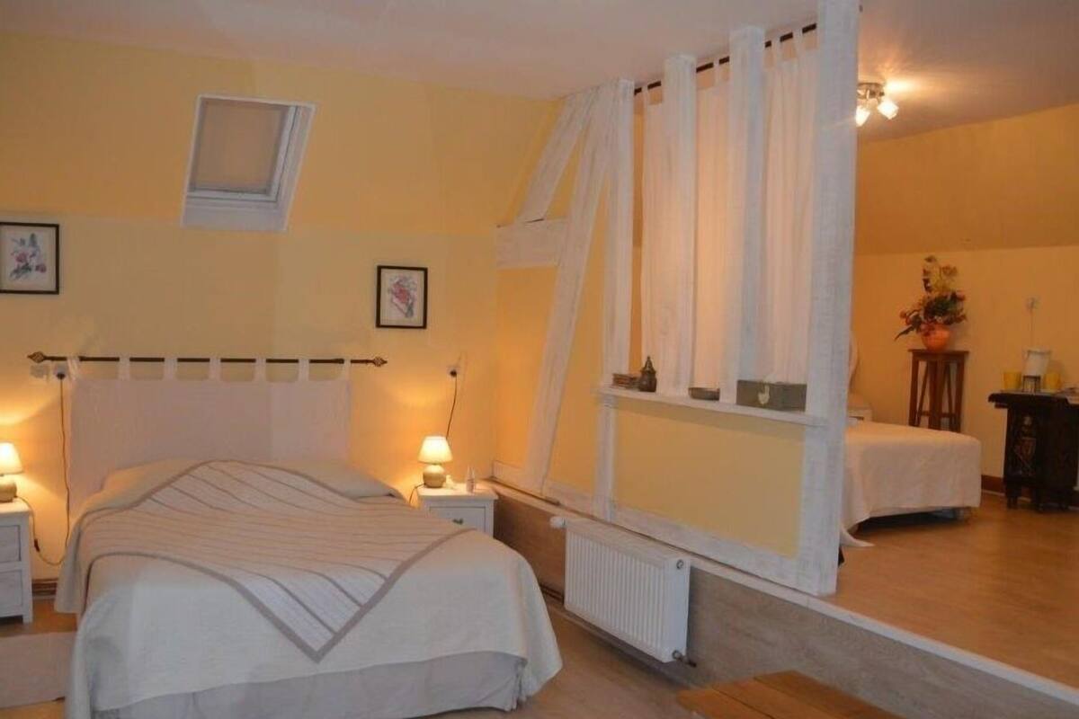 A bedroom with a large bed, bedside tables, a window with curtains, a radiator, and a small table with a plant.