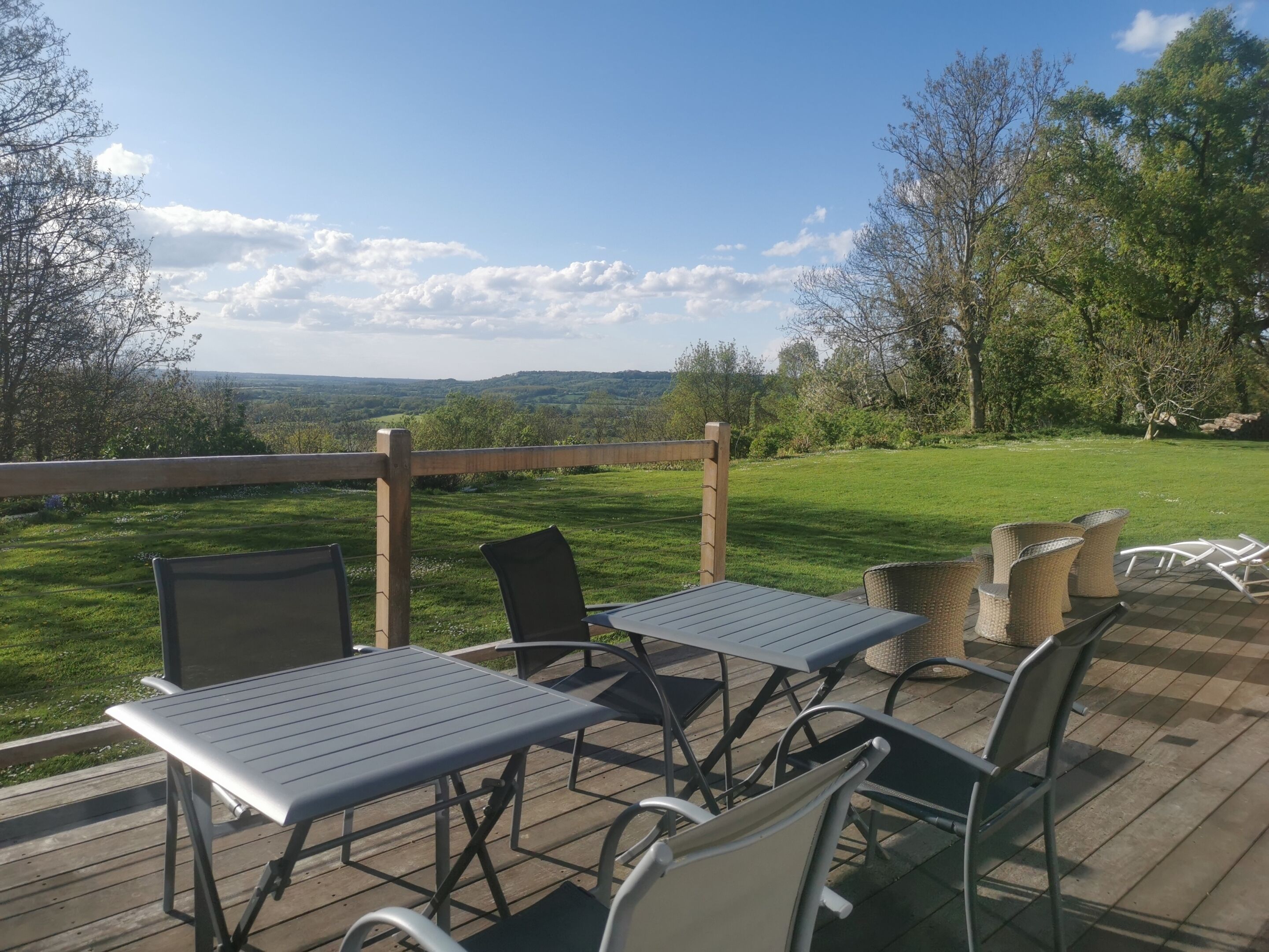 Une terrasse extérieure avec des tables et des chaises, offrant une vue sur un paysage verdoyant et des arbres.