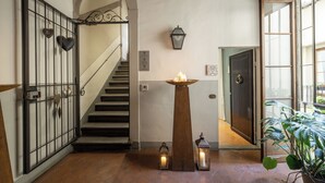 A staircase leading to a second floor, a door with a metal gate, a wall-mounted light fixture, and a potted plant. - Canto degli Scali (Florence)